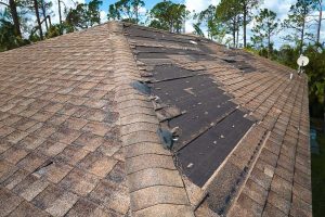 A damaged that needs roof repari. Missing shingles after a severe weather event, with a clear sky in the background.